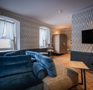 la-villetta-salon-camelia.jpg Wohnbereich mit samtblauem Sofa, gemusterten Tapeten und organisch gerundetem Schrankelement im Salon Camelia der La Villetta.